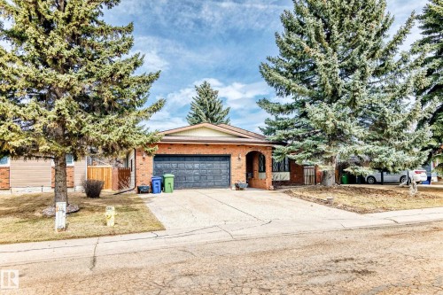 Brick exterior with a prominent arched entry, attached garage, and mature evergreen trees - 208 Willow Crescent, Wetaskiwin, AB - Outdoor