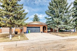 Brick exterior with a prominent arched entry, attached garage, and mature evergreen trees - 