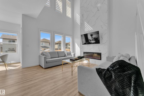The property features an open-concept living space with light wood-style flooring, a soaring two-story ceiling, and a prominent fireplace with a marble-effect finish - 7815 174 Avenue, Edmonton, AB - Indoor Photo Showing Living Room With Fireplace