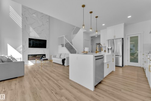 Open concept living area featuring light-toned flooring, a kitchen island with pendant lighting, and a modern fireplace with a marble-style surround - 7815 174 Avenue, Edmonton, AB - Indoor