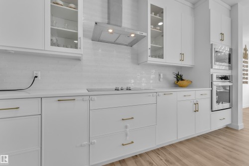 The kitchen features white cabinetry with gold hardware, a stainless steel range hood, and a built-in oven and microwave - 7815 174 Avenue, Edmonton, AB - Indoor Photo Showing Kitchen With Upgraded Kitchen