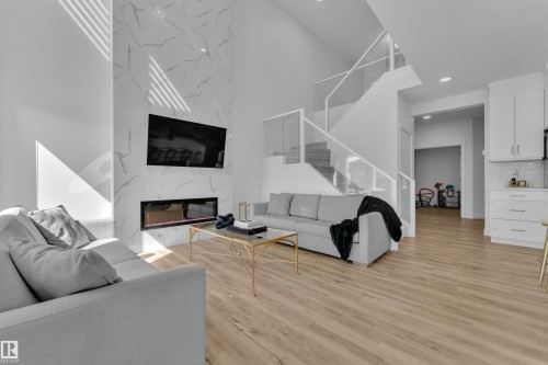 The main living area features a modern fireplace with a white marble-look surround, light-toned wooden flooring, and a contemporary staircase with glass railings - 7815 174 Avenue, Edmonton, AB - Indoor Photo Showing Living Room With Fireplace