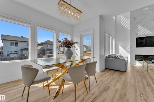 Open concept living area featuring light wood flooring, large windows, and a modern fireplace with a marble-patterned accent wall - 7815 174 Avenue, Edmonton, AB - Indoor Photo Showing Dining Room