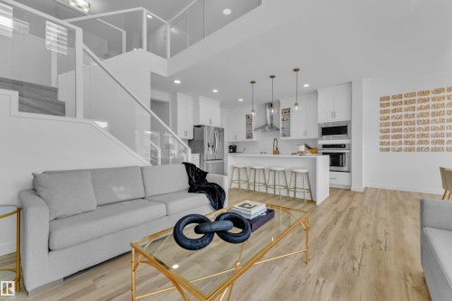 The property features an open concept living area with light-colored flooring, a modern kitchen with white cabinetry and stainless steel appliances, and a staircase with glass railings - 7815 174 Avenue, Edmonton, AB - Indoor