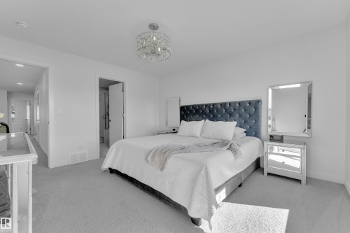 This room features light-colored walls and carpeting, a crystal chandelier, and a wide entryway visible in the background - 7815 174 Avenue, Edmonton, AB - Indoor Photo Showing Bedroom