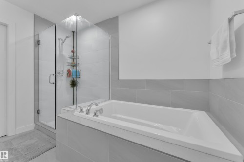 Bathroom featuring a built-in bathtub with chrome fixtures and a glass-enclosed shower with a tiled surround - 7815 174 Avenue, Edmonton, AB - Indoor Photo Showing Bathroom
