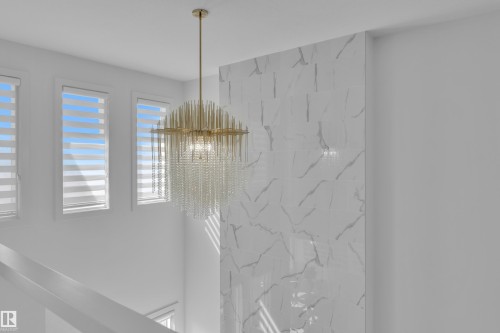 This space features a modern chandelier with gold accents and clear glass elements, set against a wall with a white and grey marble-look finish - 7815 174 Avenue, Edmonton, AB - Indoor Photo Showing Other Room