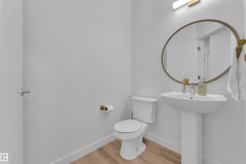 This bathroom features light-toned flooring, a pedestal sink, a toilet, and a circular mirror with a gold-toned frame - 7815 174 Avenue, Edmonton, AB - Indoor Photo Showing Bathroom