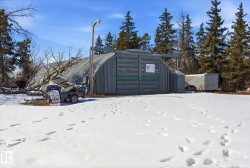 Quonset building with a metal exterior, overhead lighting fixture, and surrounding evergreen trees - 