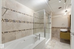 Full bathroom featuring a combination tub and shower with glass enclosure, beige ceramic wall tile, mosaic tile accents, and a vessel sink on a wood-finish vanity - 