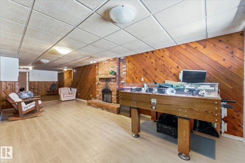 Spacious recreation room featuring wood-finish flooring, a brick fireplace with hearth, and wood paneling - 25750 18 Street, Edmonton, AB - Indoor Photo Showing Other Room