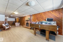 Spacious recreation room featuring wood-finish flooring, a brick fireplace with hearth, and wood paneling - 