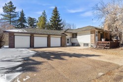 Exterior featuring a three-car garage with white doors, brick accents, white siding, and a multi-level wooden deck - 