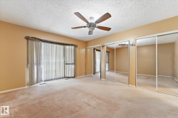 Spacious room featuring neutral carpeting, a ceiling fan, and a large window with vertical blinds - 