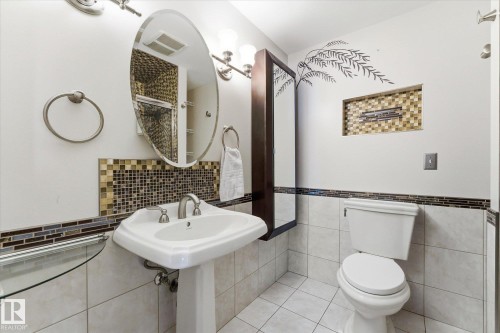Bathroom featuring a white pedestal sink with brushed nickel faucet, an oval mirror, and an adjacent toilet - 25750 18 Street, Edmonton, AB - Indoor Photo Showing Bathroom