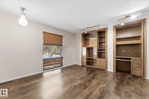 Wood-finish flooring throughout, featuring a window with wood blinds, and built-in cabinetry with shelving and desk space - 25750 18 Street, Edmonton, AB - Indoor Photo Showing Other Room
