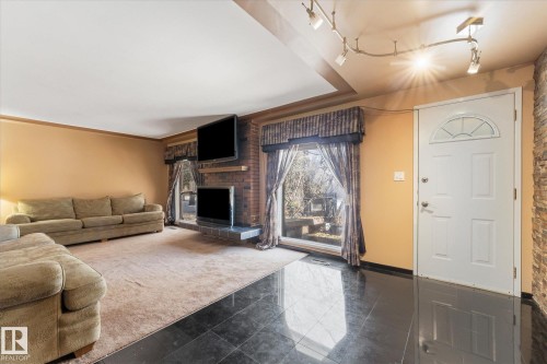 Living area featuring black tile flooring, a white paneled entry door with a decorative fanlight, and a brick fireplace - 25750 18 Street, Edmonton, AB - Indoor Photo Showing Living Room With Fireplace