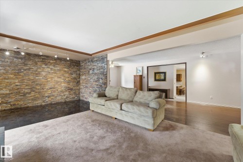 Living area featuring a stone veneer accent wall with track lighting, contrasting with light-toned carpeting and dark tile flooring - 25750 18 Street, Edmonton, AB - Indoor Photo Showing Living Room