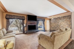 Interior space featuring a brick fireplace surround with a dark mantel, a large picture window, a stone accent wall with track lighting, and a white entry door with an arched glass insert - 
