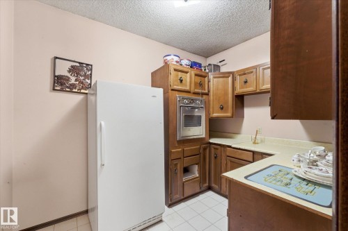 Kitchen featuring wood cabinetry, built-in wall oven, light-toned countertops, and white tile flooring - 25750 18 Street, Edmonton, AB - Indoor