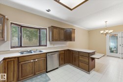 Kitchen featuring wood cabinetry, white countertops, a stainless steel dishwasher, and a double basin sink - 