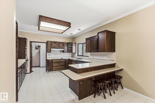 Kitchen featuring extensive dark wood cabinetry, light-toned countertops, and a built-in breakfast bar - 25750 18 Street, Edmonton, AB - Indoor Photo Showing Kitchen