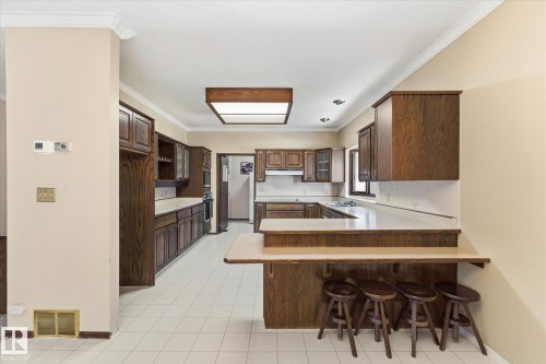 Kitchen featuring extensive wood-finish cabinetry, white tiled flooring, a built-in breakfast bar, recessed lighting, and a tray ceiling with central lighting fixture - 25750 18 Street, Edmonton, AB - Indoor Photo Showing Kitchen