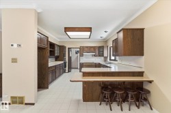 Kitchen featuring extensive wood-finish cabinetry, white tiled flooring, a built-in breakfast bar, recessed lighting, and a tray ceiling with central lighting fixture - 