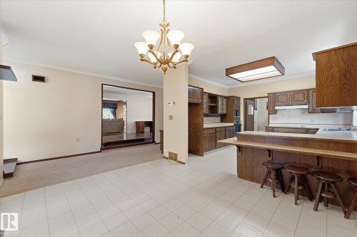 Spacious kitchen and dining area featuring wood-finish cabinetry, white tile flooring, and a breakfast bar - 25750 18 Street, Edmonton, AB - Indoor