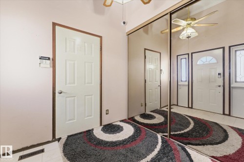Interior entryway featuring full-height mirrored closet doors, a ceiling fan with integrated lighting, and a six-panel interior door with wood-finish trim - 25750 18 Street, Edmonton, AB - Indoor Photo Showing Other Room