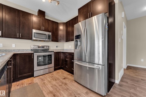 Kitchen featuring dark wood cabinetry, stainless steel appliances, granite-style countertops, wood-finish flooring, and recessed lighting - 2526 19A Avenue, Edmonton, AB - Indoor Photo Showing Kitchen With Stainless Steel Kitchen