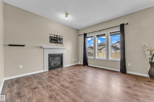 Living area featuring a fireplace with a tiled surround and mantel, wood-finish flooring, and a wall-mounted shelving unit - 2526 19A Avenue, Edmonton, AB - Indoor Photo Showing Living Room With Fireplace
