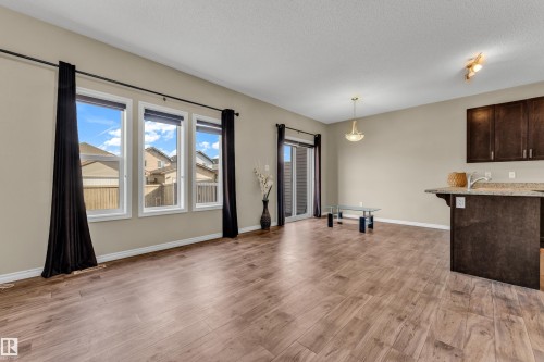 Spacious living area featuring wood-finish flooring, a wall of three windows, and a glass sliding door - 2526 19A Avenue, Edmonton, AB - Indoor