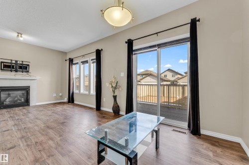 Living area featuring wood-finish flooring, a built-in fireplace with a tiled surround, a multi-pane window, and sliding glass doors leading to a private deck - 2526 19A Avenue, Edmonton, AB - Indoor Photo Showing Living Room With Fireplace