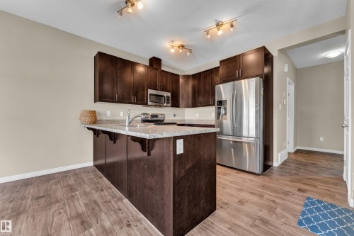 Kitchen featuring dark wood cabinetry, stainless steel appliances, granite-style countertops, and wood-finish flooring - 2526 19A Avenue, Edmonton, AB - Indoor Photo Showing Kitchen With Stainless Steel Kitchen