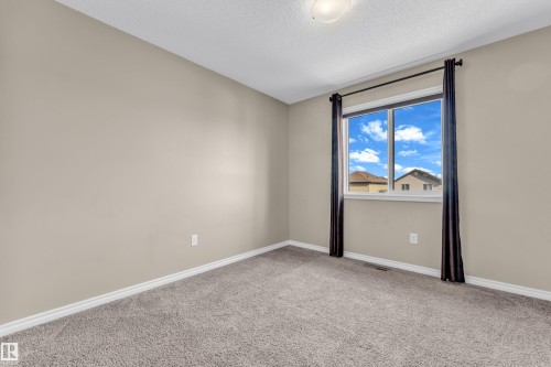 Bright room featuring a prominent window with dark draperies, light beige painted walls, neutral toned carpet flooring, and white baseboards - 2526 19A Avenue, Edmonton, AB - Indoor Photo Showing Other Room