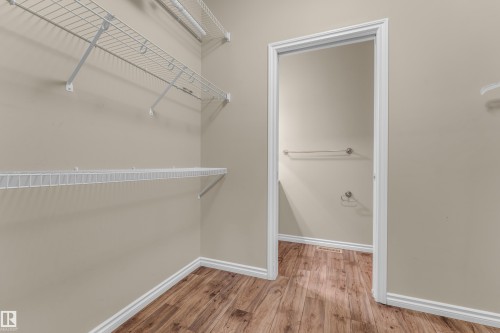 Walk-in closet featuring wire shelving, wire hanging rods, neutral wall paint, white baseboards, and wood-finish flooring - 2526 19A Avenue, Edmonton, AB - Indoor With Storage