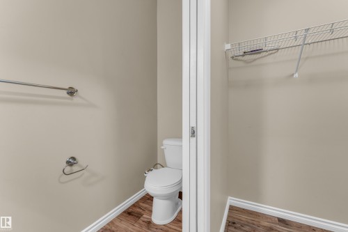 Powder room with a white toilet, chrome towel bar, and wood-finish flooring - 2526 19A Avenue, Edmonton, AB - Indoor Photo Showing Bathroom