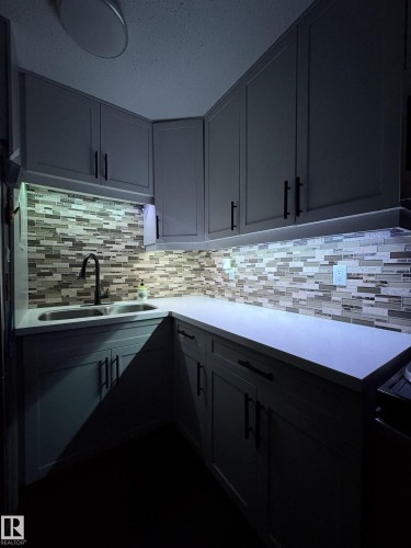 Kitchen featuring light gray cabinetry with black hardware, mosaic tile backsplash, solid surface countertops, and an undermount double basin sink with a black gooseneck faucet - 79 Akinsdale Gardens, St. Albert, AB - Indoor Photo Showing Kitchen With Double Sink With Upgraded Kitchen