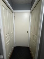 Hallway with a solid panel door, two bi-fold doors, and a dark carpeted floor - 