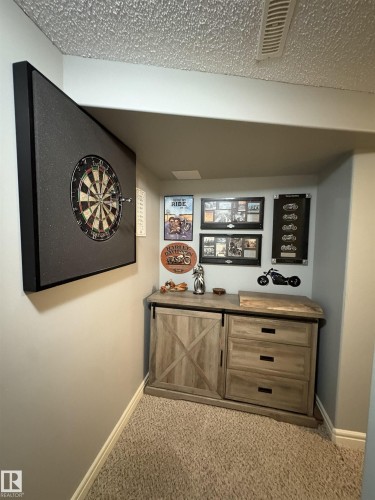Carpeted recreation area featuring a built-in dartboard, recessed lighting, and a wood-finish cabinet with sliding barn door accent and drawer storage - 79 Akinsdale Gardens, St. Albert, AB - Indoor Photo Showing Other Room