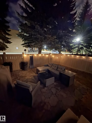 Private patio space featuring a flagstone surface, wood privacy fencing, and mature evergreen trees - 79 Akinsdale Gardens, St. Albert, AB - 