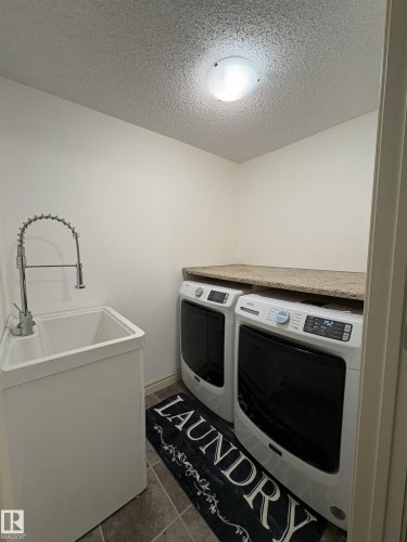 Dedicated laundry space featuring a utility sink with a high-arc faucet, tiled flooring, and a durable countertop - 79 Akinsdale Gardens, St. Albert, AB - Indoor Photo Showing Laundry Room