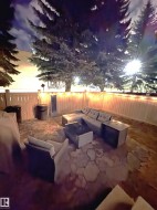 Outdoor patio featuring flagstone flooring, a privacy fence with string lighting, and mature evergreen trees - 