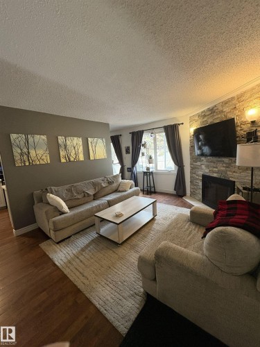Living area featuring wood-finish flooring, a stacked stone accent wall, and a fireplace with a black insert - 79 Akinsdale Gardens, St. Albert, AB - Indoor Photo Showing Living Room With Fireplace