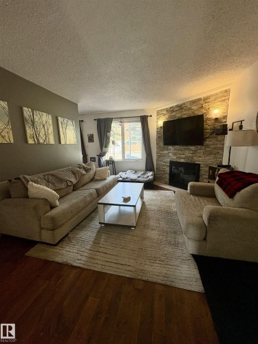 Living area featuring wood-finish flooring and a corner fireplace with a stacked stone surround - 79 Akinsdale Gardens, St. Albert, AB - Indoor Photo Showing Living Room With Fireplace