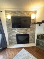 Stacked stone fireplace with a black insert, white tile hearth, and two wall sconces - 