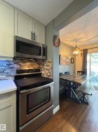 Kitchen featuring stainless steel appliances, light-toned cabinetry with dark hardware, and a mosaic tile backsplash - 