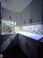 L-shaped kitchen with light-toned cabinetry and matte black hardware, featuring a double basin stainless steel sink and a mosaic tile backsplash - 