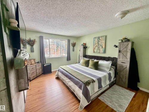 Spacious bedroom featuring wood-finish flooring, a large window, light green painted walls, and built-in closet cabinetry - 3520 17B Avenue, Edmonton, AB - Indoor Photo Showing Bedroom